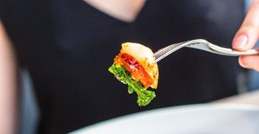 Her ser man et foto af en kvinde, der spiser mad. Kameraet fokuserer på hendes gaffel med en bid mad